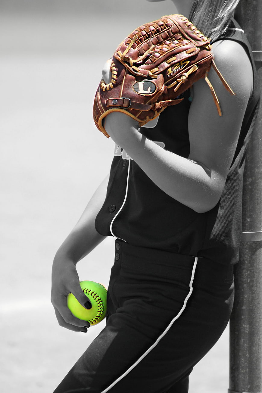 Softball Player in Black Uniform Holding Green Ball with Leather Glove