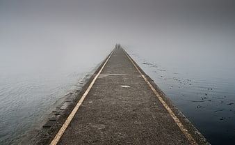 Foggy pier walkway disappearing into misty ocean horizon
