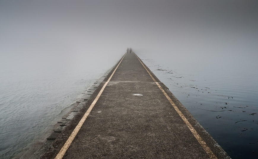 Foggy pier walkway disappearing into misty ocean horizon