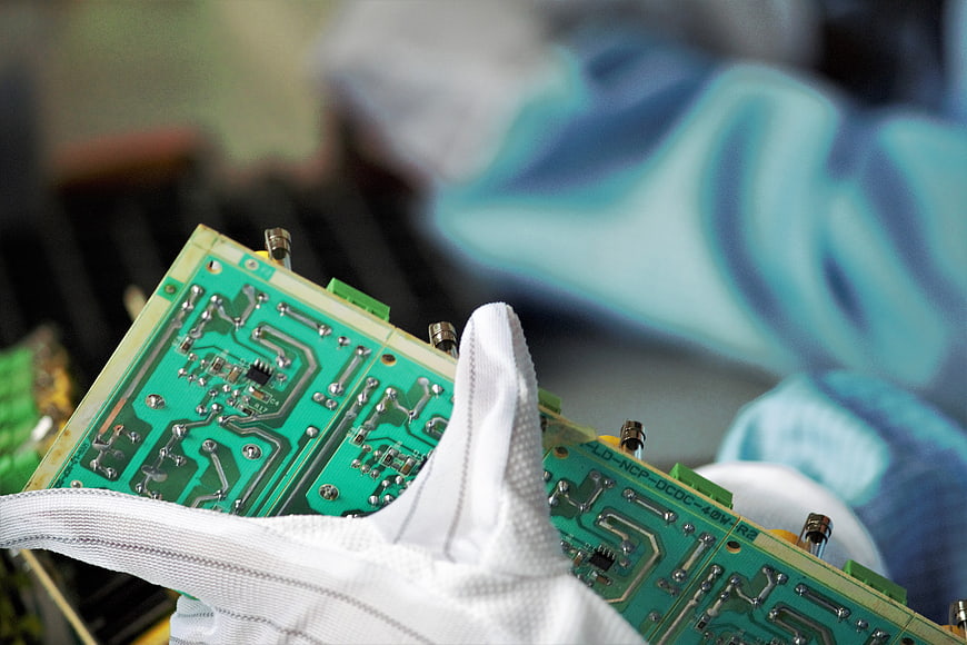Gloved Hand Holding Green Circuit Board in Electronics Lab