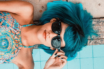 Woman with blue hair and sunglasses by pool