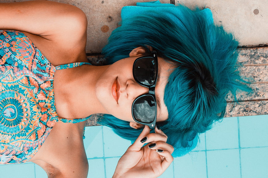 Woman with blue hair and sunglasses by pool