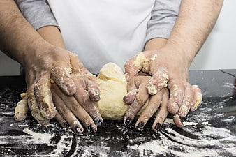 Couple's hands kneading dough together on a floured black surface