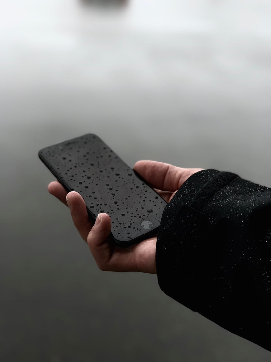 Hand holding wet smartphone in rain
