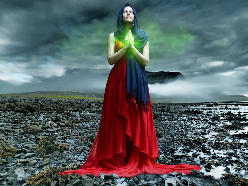 Woman in Red Dress Praying with Green Light on Rocky Beach
