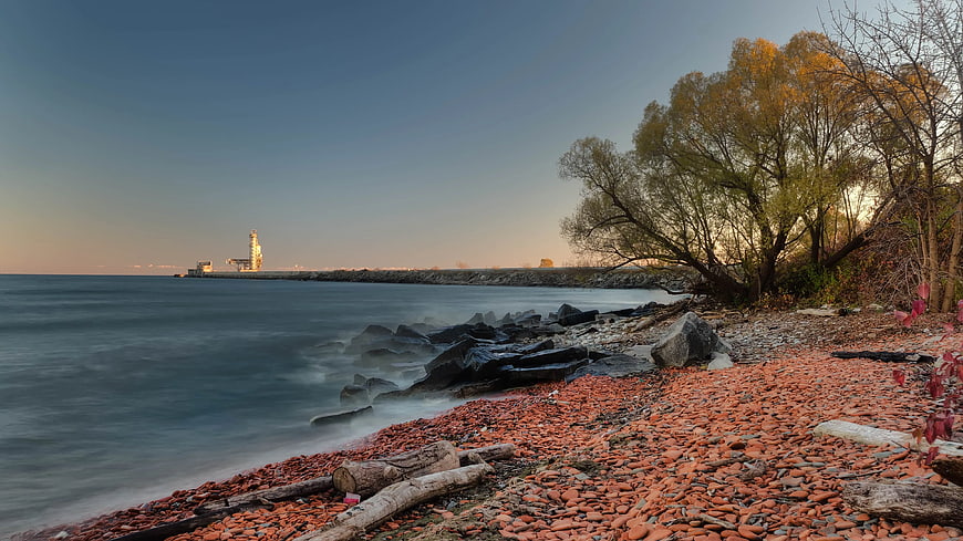 Red Pebble Beach with Lighthouse and Autumn Trees