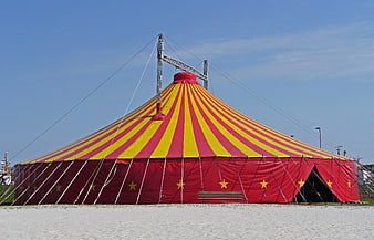 Red and yellow striped circus tent on a sandy beach under a clear blue sky