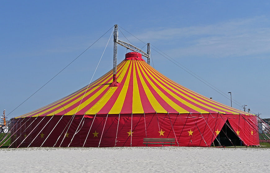 Red and yellow striped circus tent on a sandy beach under a clear blue sky
