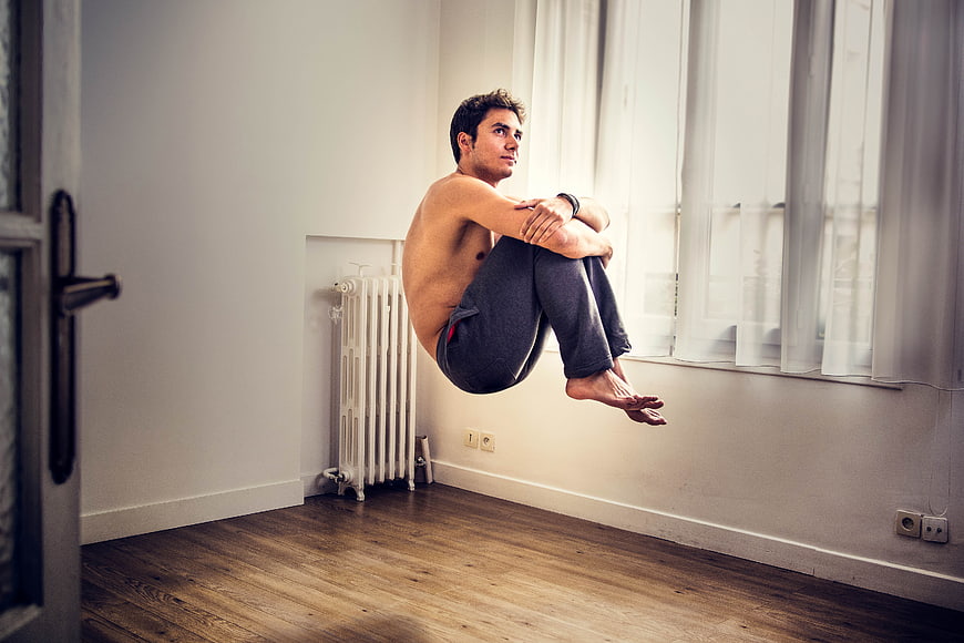Shirtless Man Floating in Meditation Pose in Minimalist Room