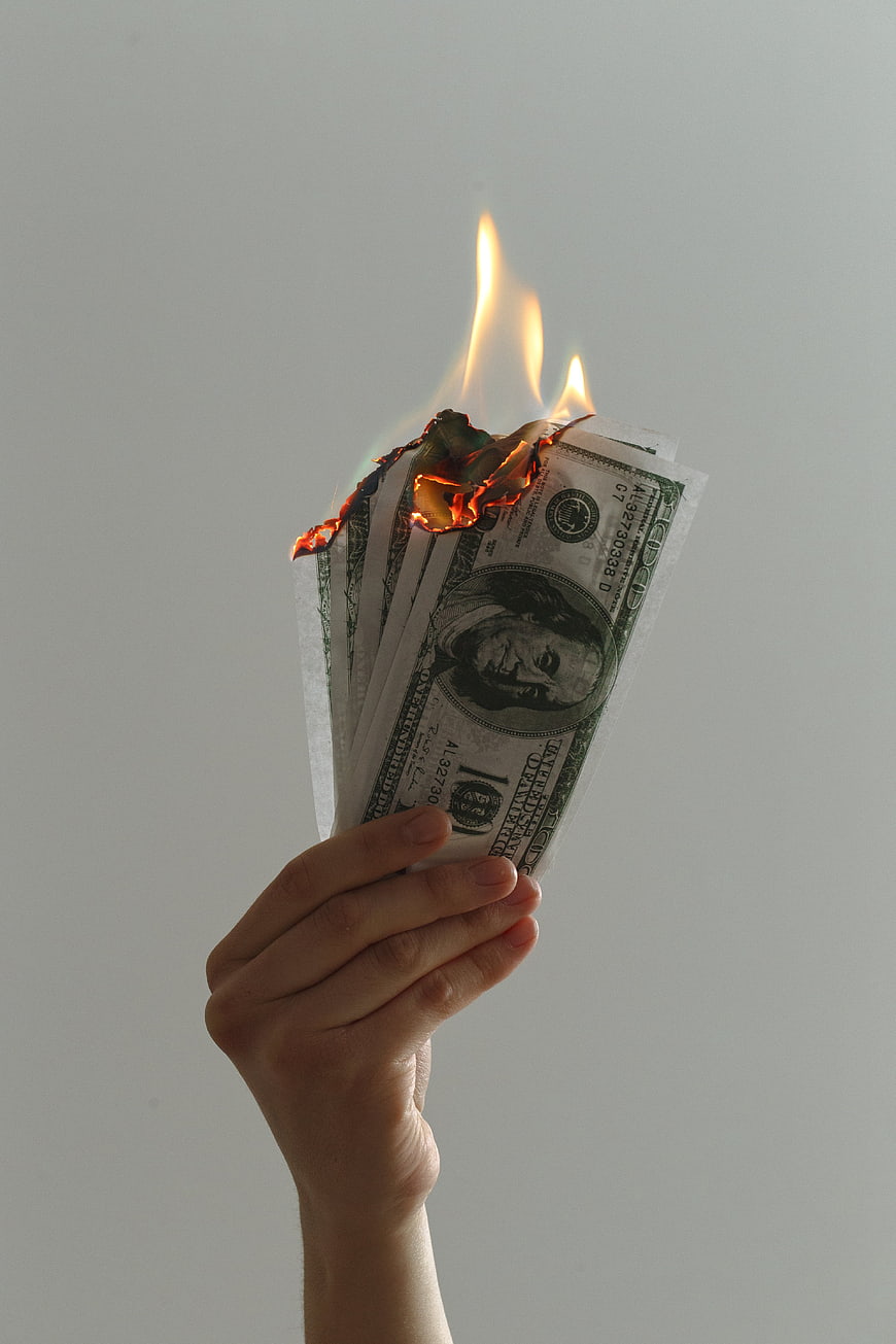 Hand Holding Burning US Dollar Bills on White Background
