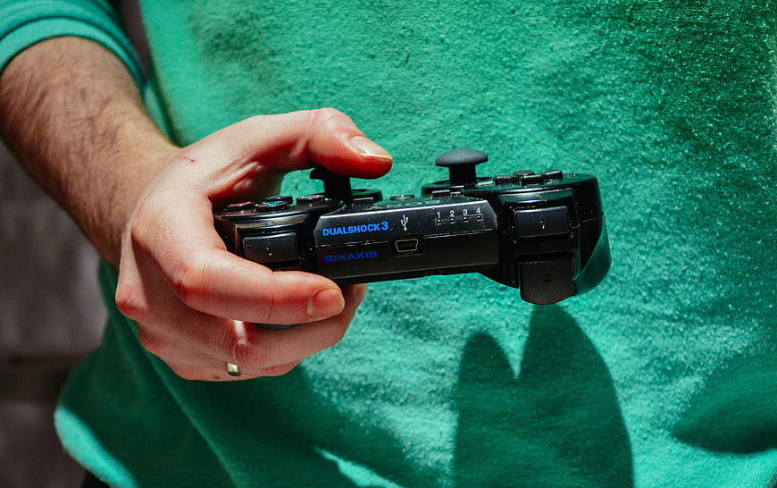 Hand holding black DualShock 3 controller against green shirt