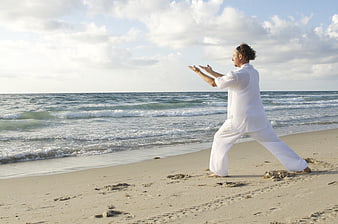 Man practicing Tai Chi on sandy beach with ocean waves