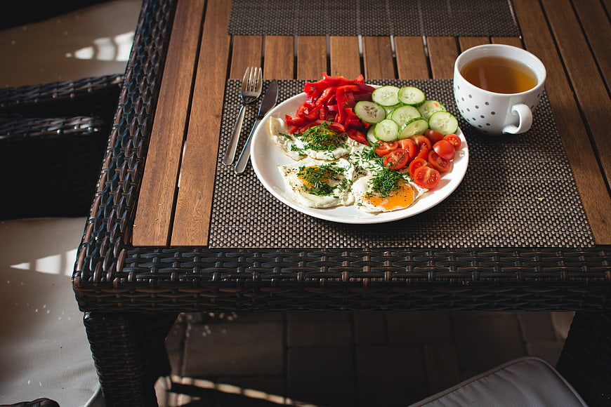 Healthy breakfast with fried eggs, fresh vegetables, and tea on a wooden table