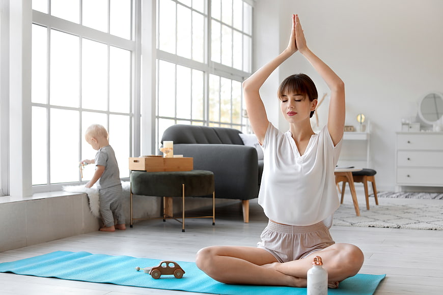 Mother practicing yoga at home with toddler playing nearby