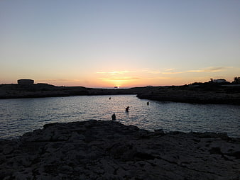 Sunset over rocky coastal inlet with calm water