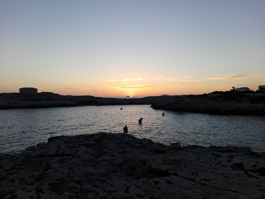 Sunset over rocky coastal inlet with calm water
