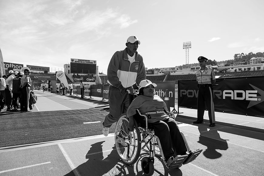 Black and white photo of a man pushing a woman in a wheelchair at a stadium