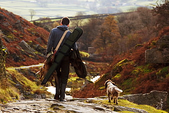 Hunter with shotgun and dog walking in autumn countryside
