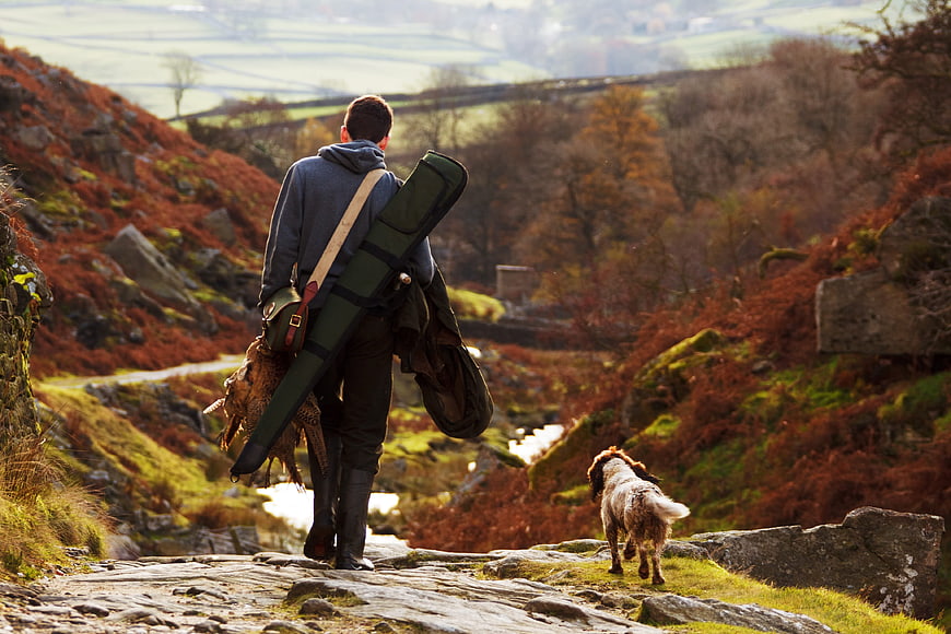 Hunter with shotgun and dog walking in autumn countryside