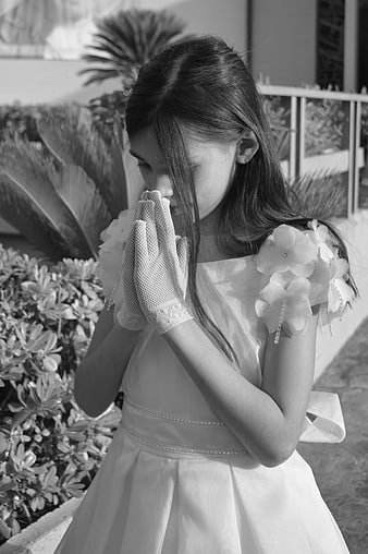 Young girl in white dress praying with lace gloves outdoors