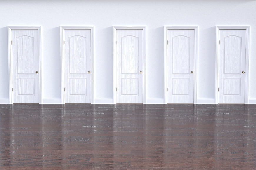Five white doors in a row on a white wall with dark floor