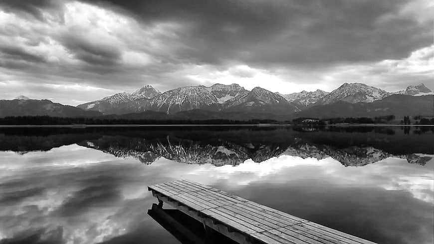 Black and white landscape of wooden dock on lake with mountains