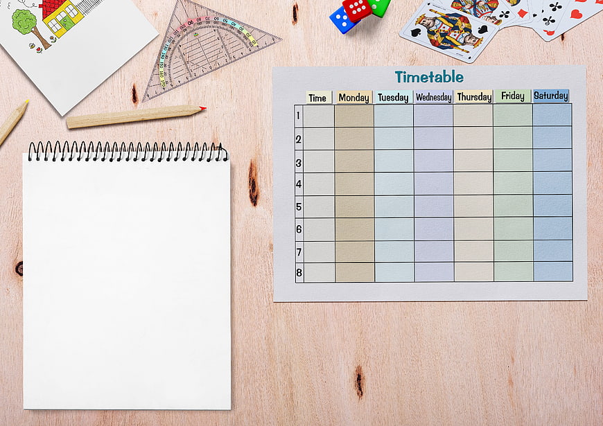 Flat lay of school timetable, notebook, and stationery on wooden desk