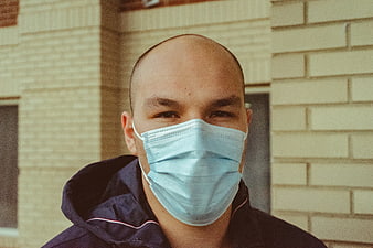 Bald man wearing blue surgical mask outdoors