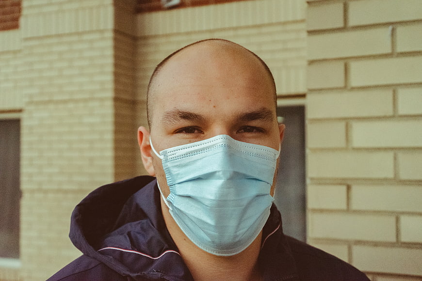 Bald man wearing blue surgical mask outdoors