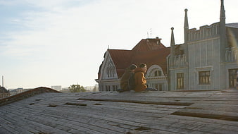 Two people sitting on a wooden rooftop with city architecture