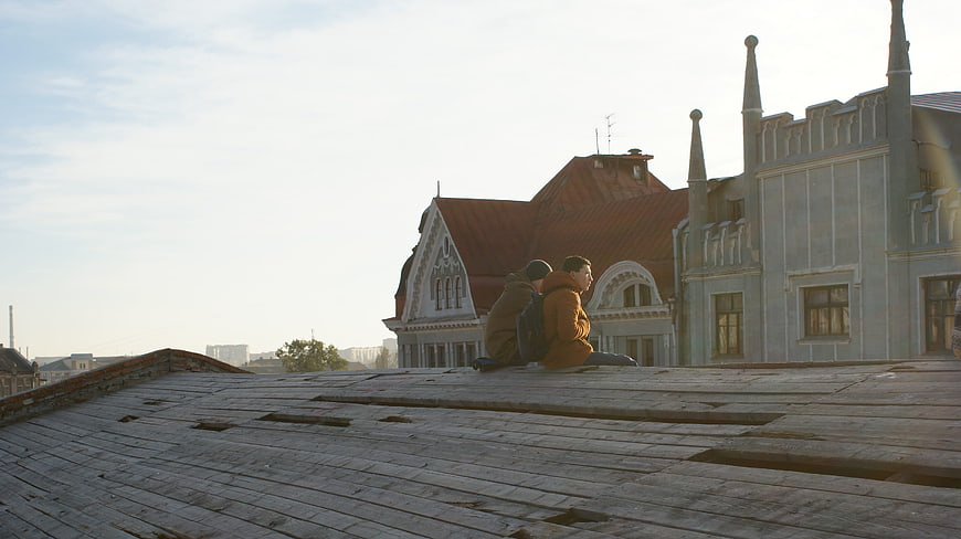 Two people sitting on a wooden rooftop with city architecture
