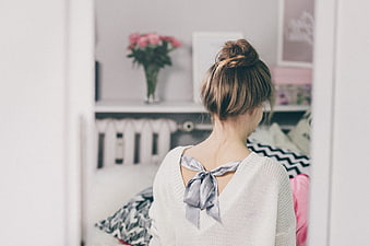 Woman with messy bun hairstyle looking at bedroom shelf
