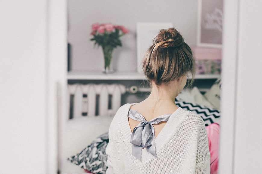 Woman with messy bun hairstyle looking at bedroom shelf