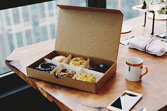 Box of assorted donuts on wooden table with coffee