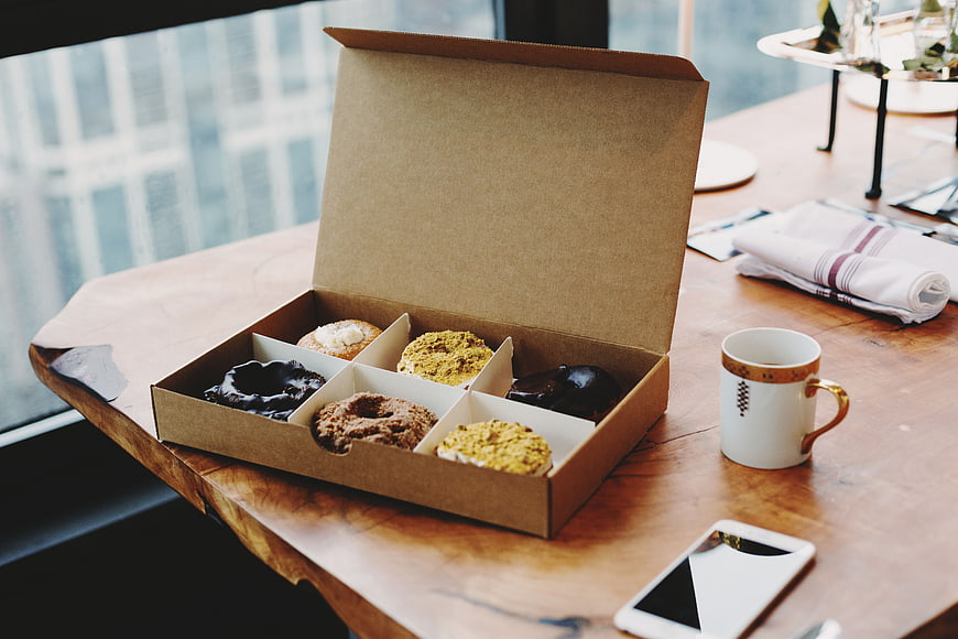 Box of assorted donuts on wooden table with coffee