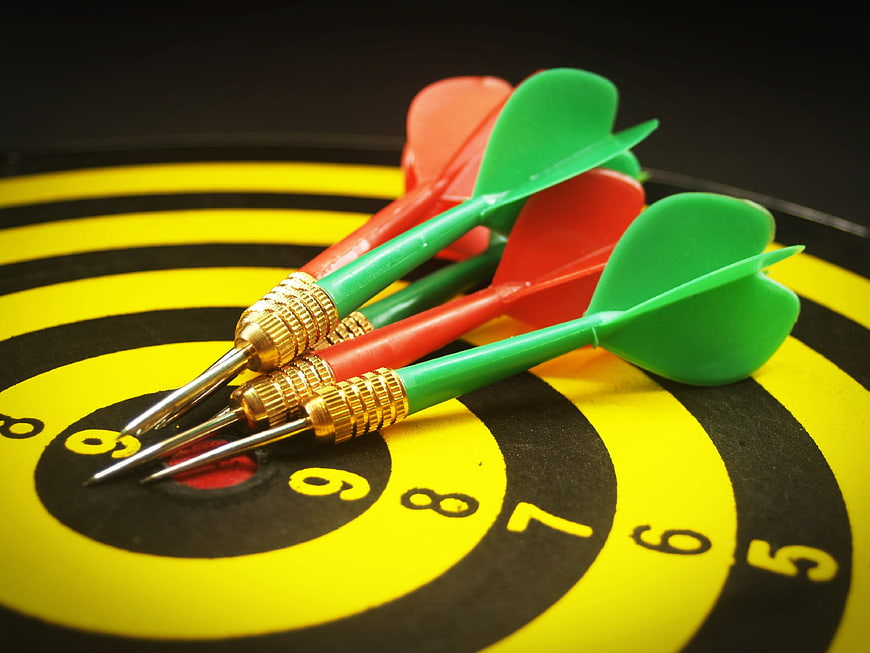 Close-up of red and green darts hitting the bullseye of a dartboard