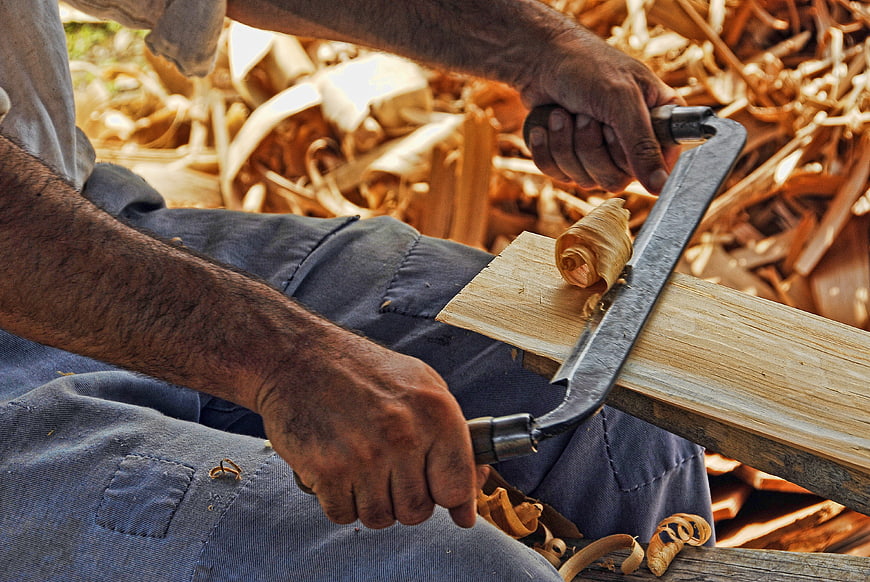 Carpenter using hand plane on wood plank