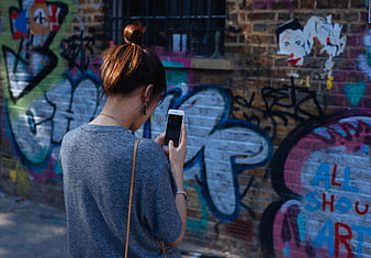 Woman using smartphone in front of colorful graffiti wall