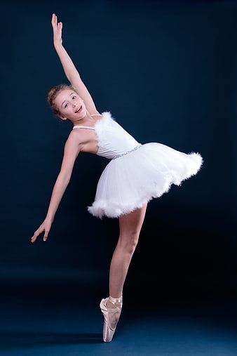 Young ballerina performing en pointe in white tutu against dark blue background