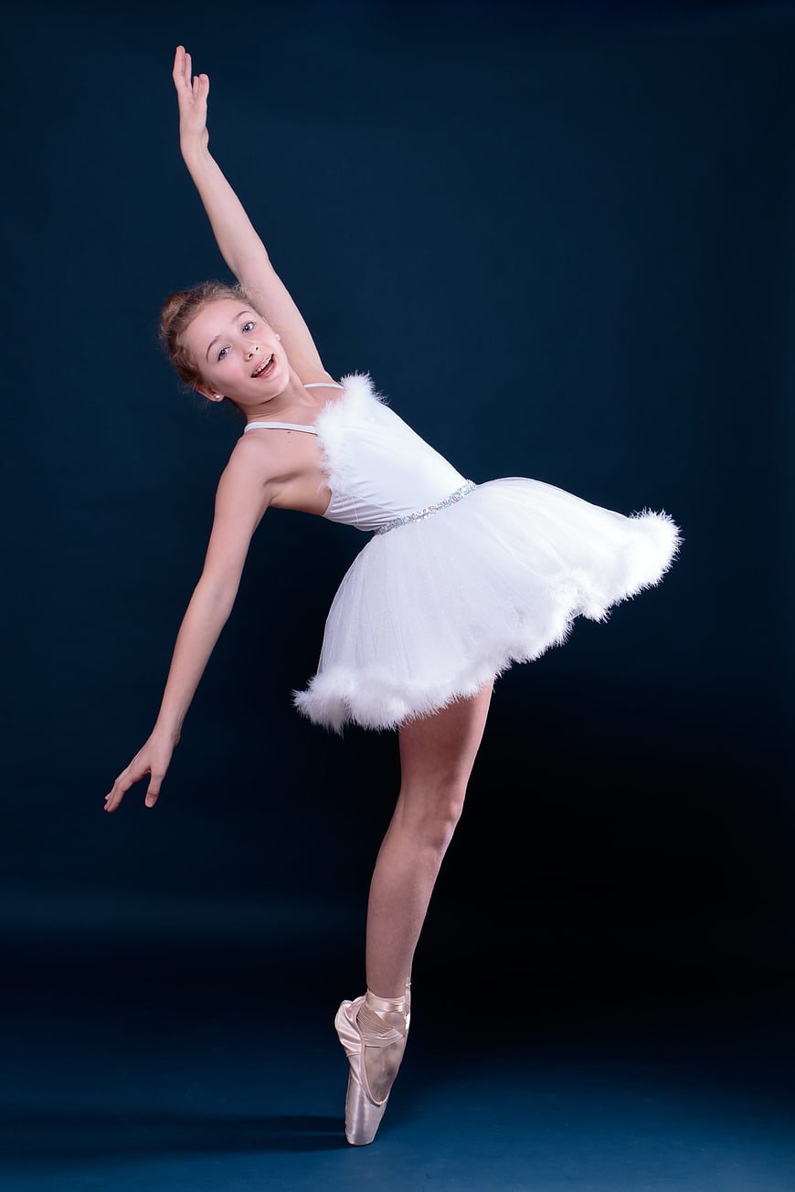 Young ballerina performing en pointe in white tutu against dark blue background