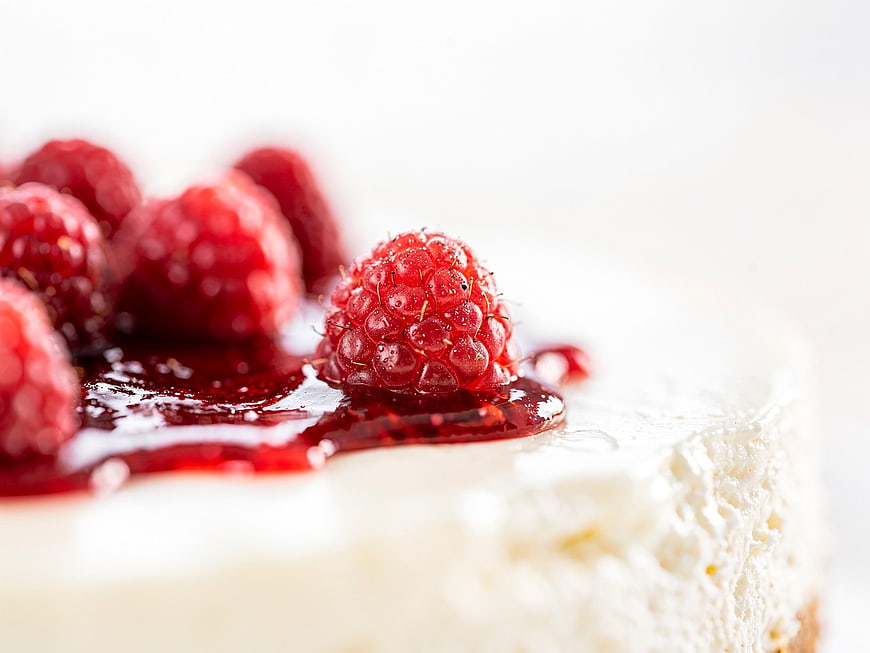 Close-up of creamy cheesecake with fresh raspberries and red glaze