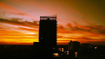 Silhouette of unfinished skyscraper against vibrant orange sunset sky