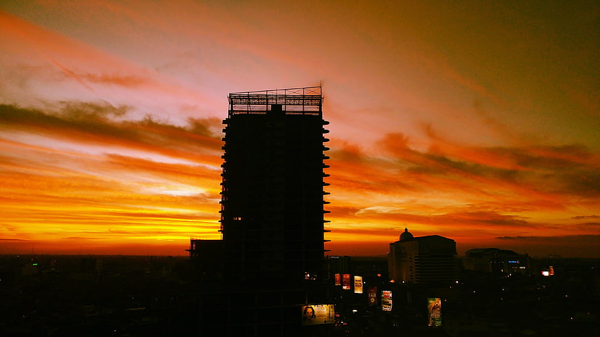 Silhouette of unfinished skyscraper against vibrant orange sunset sky