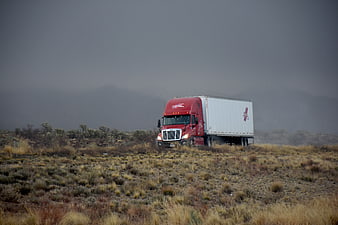 Red semi-truck driving through desert landscape in foggy weather