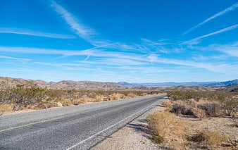 Empty Desert Highway Stretching to Distant Mountains Under Blue Sky