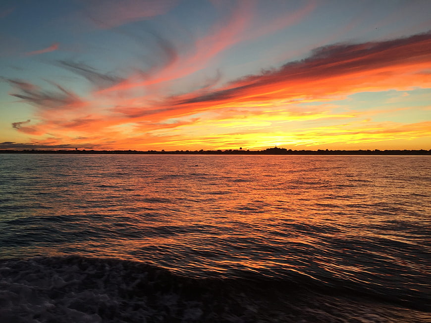 Vibrant Orange Sunset Over Ocean Water with Distant Shoreline
