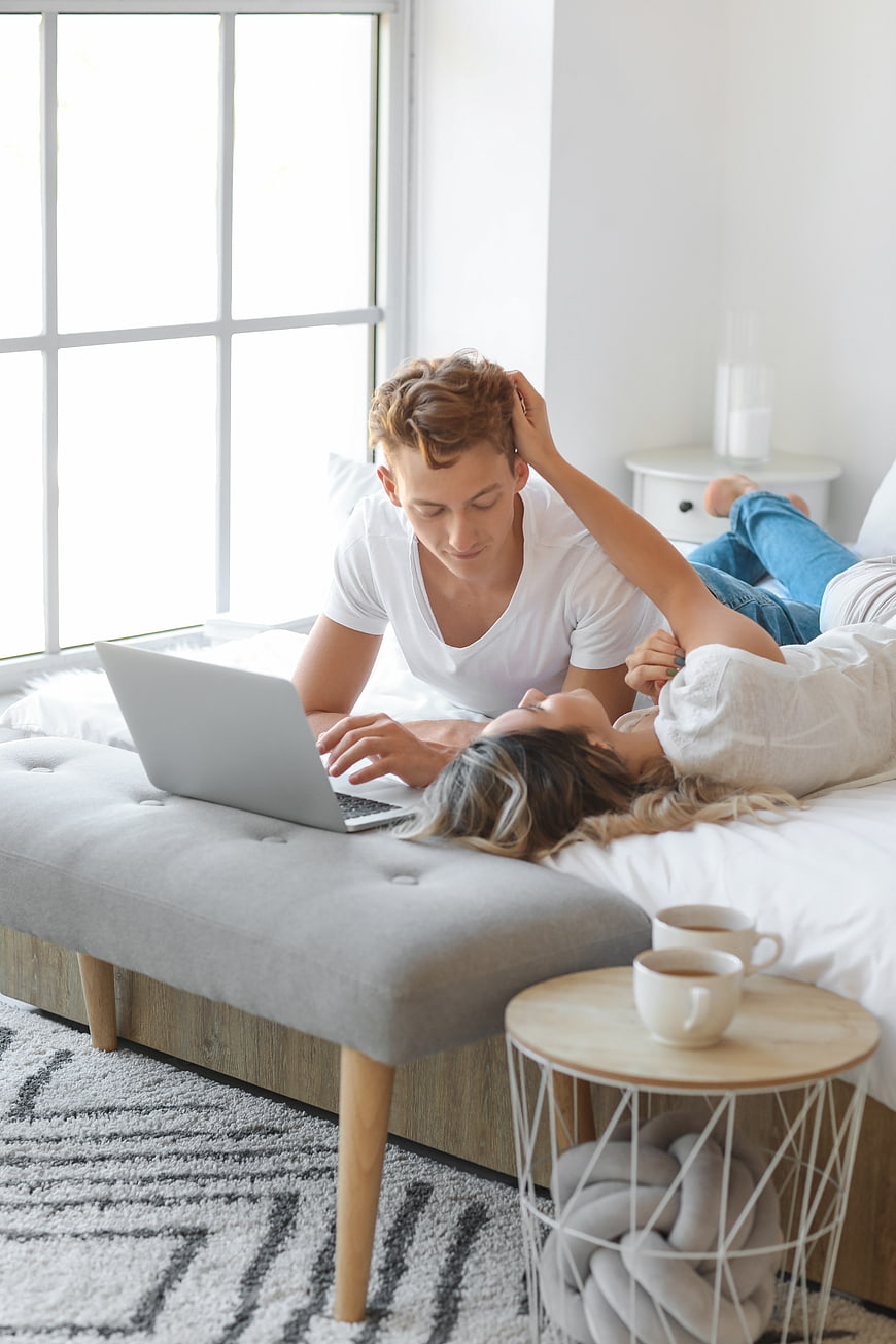 Young couple relaxing in bed with laptop and coffee