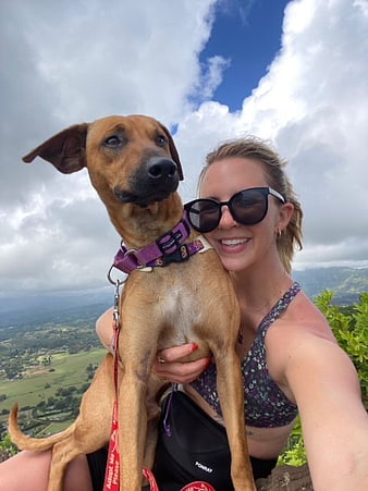 Woman holding brown dog on mountain hiking trail