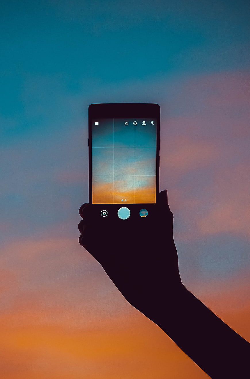 Hand holding smartphone capturing sunset sky silhouette