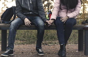 Couple holding hands on park bench with alcohol bottles